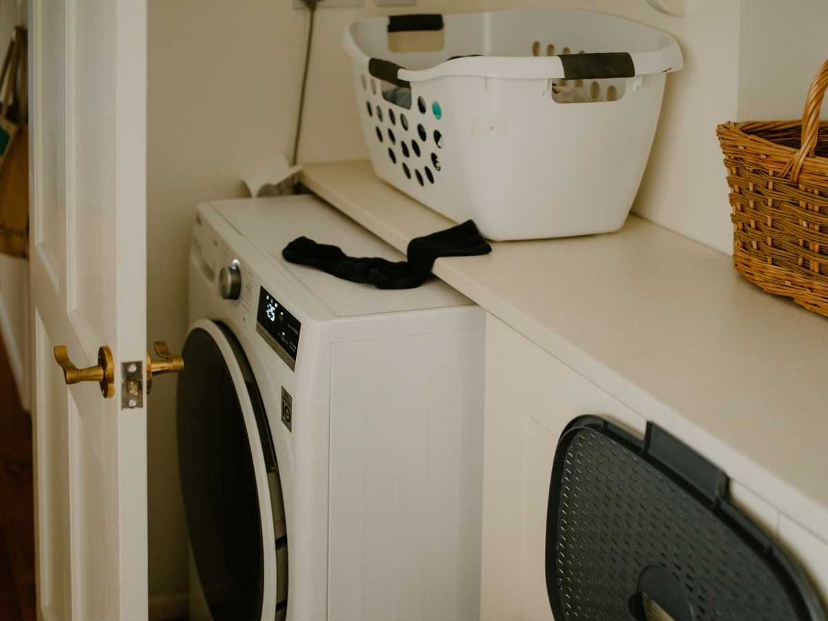 A front-load washer in a home laundry room with a laundry basket above it