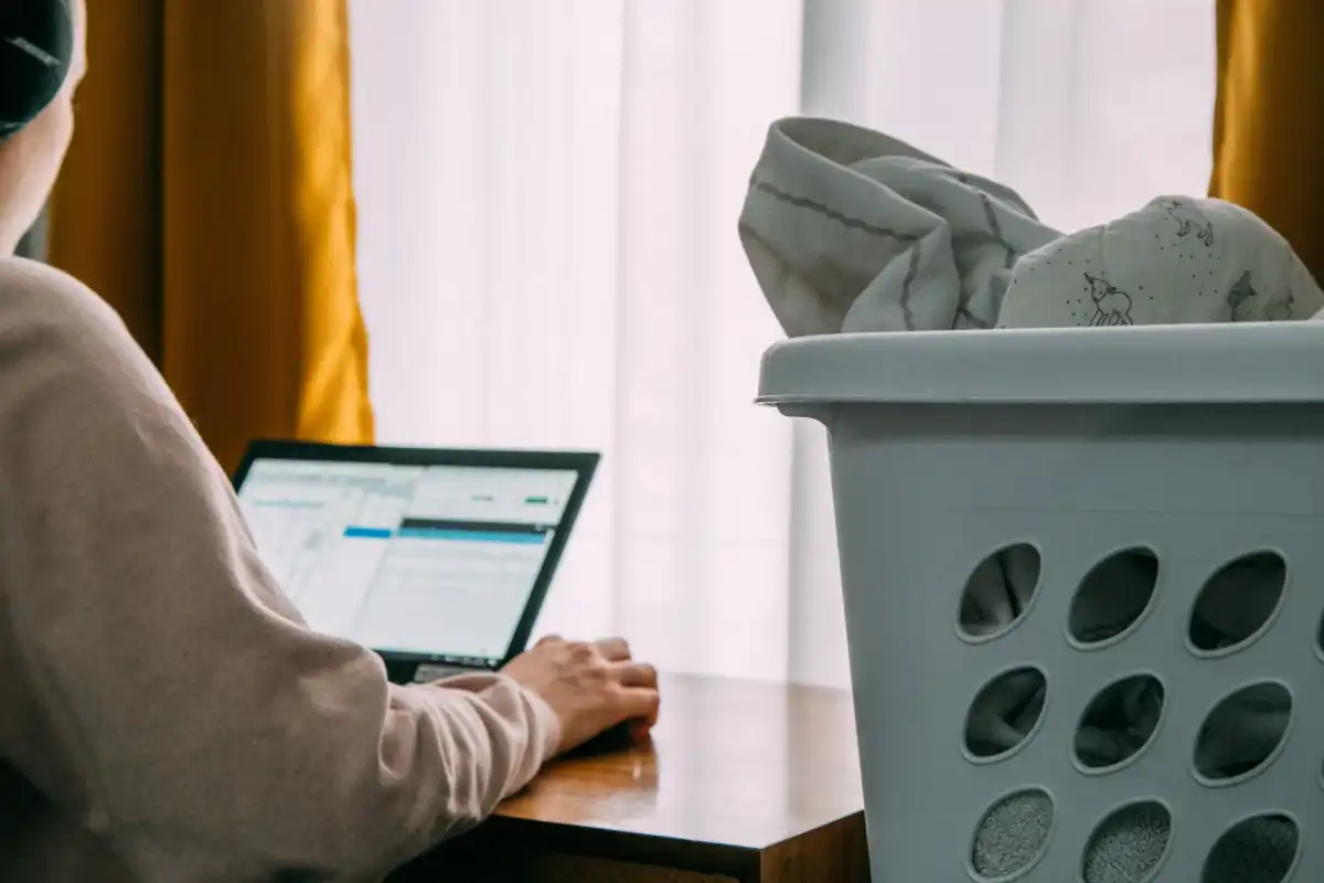 Person working on a laptop next to a full laundry basket