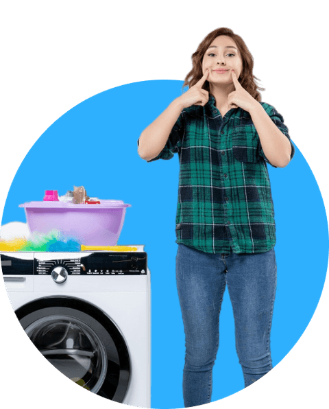 A smiling woman beside a washing machine and a basket of laundry
